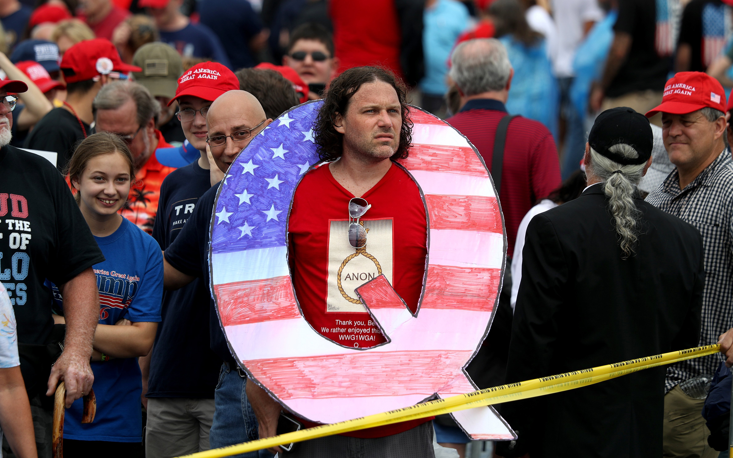 Image:  David Reinert holds a large “Q” sign while waiting to see Trump