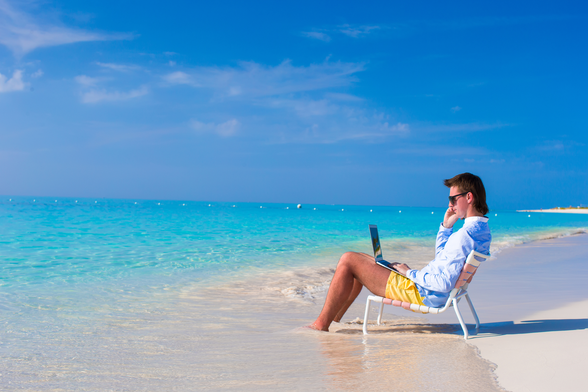 Young man with laptop and cell phone on tropical beach